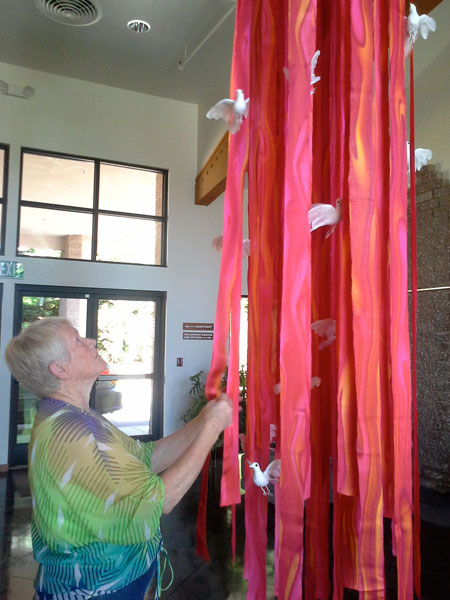 Peace Lutheran Church’s liturgical artist, Ingrid Dreyer, arranges a floating sculpture in the church atrium in preparation for the festival of Pentecost, one of the three great holy days along with Easter and Christmas. The doves are a symbol of the Holy Spirit, and the red evokes flame, another Pentecost symbol.