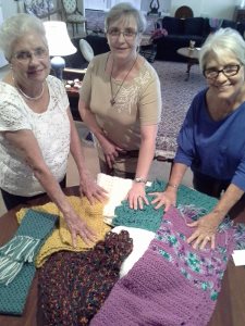 Bobbi Meyer, Pastor Eileen Smith Le Van and Judy Kenney pray over shawls they have knitted and crocheted.