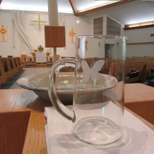 A glass pitcher in front of a ceramic baptismal font, with the church Sanctuary in the background.