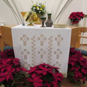 Altar with white cloth, Holy Communion vessels, and red poinsettias at the base.